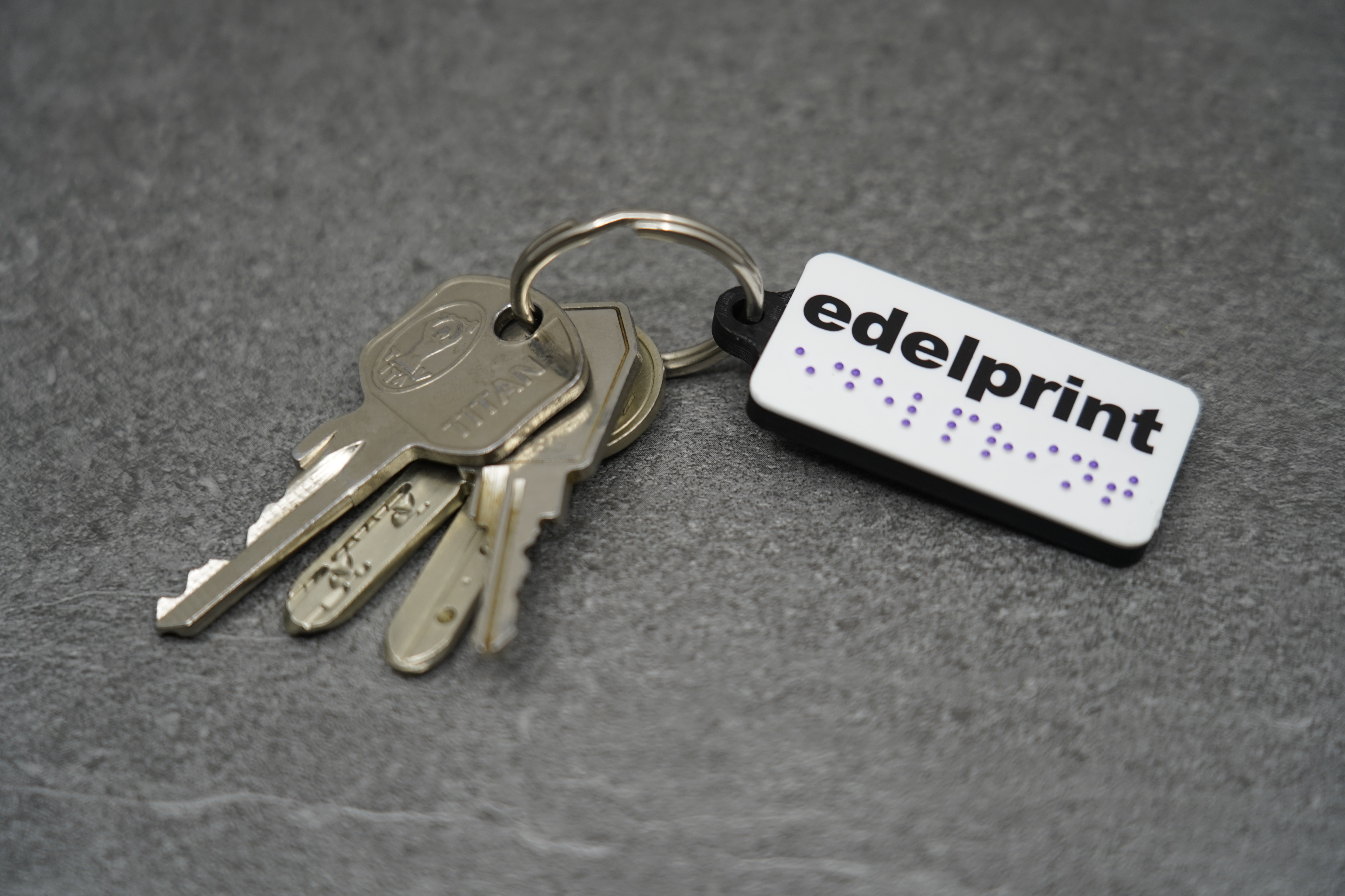 Bedruckter Schlüsselanhänger mit edelprint-Logo und lila Braille-Punkten